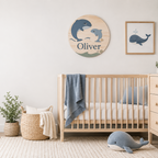 Personalized round wooden name sign and framed whale print above a wooden crib